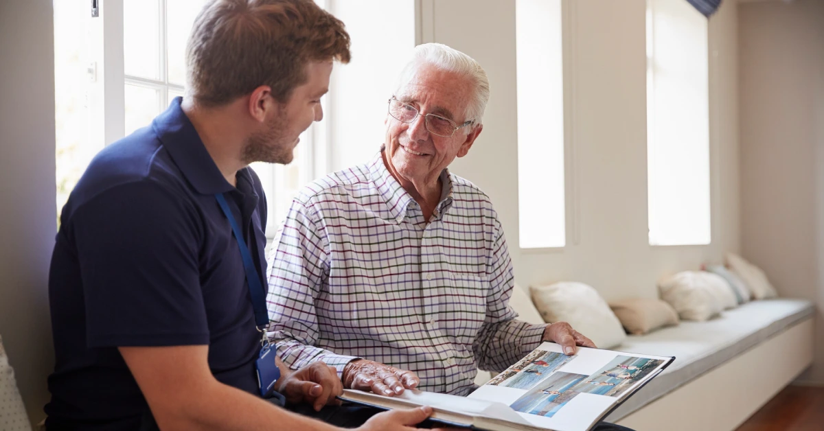 Senior man sitting looking at photo album with male nurse